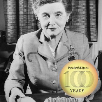 Woman sits at table, slicing bread, wearing a buttoned suit. A "Reader's Digest 100 Years" emblem overlays the image.