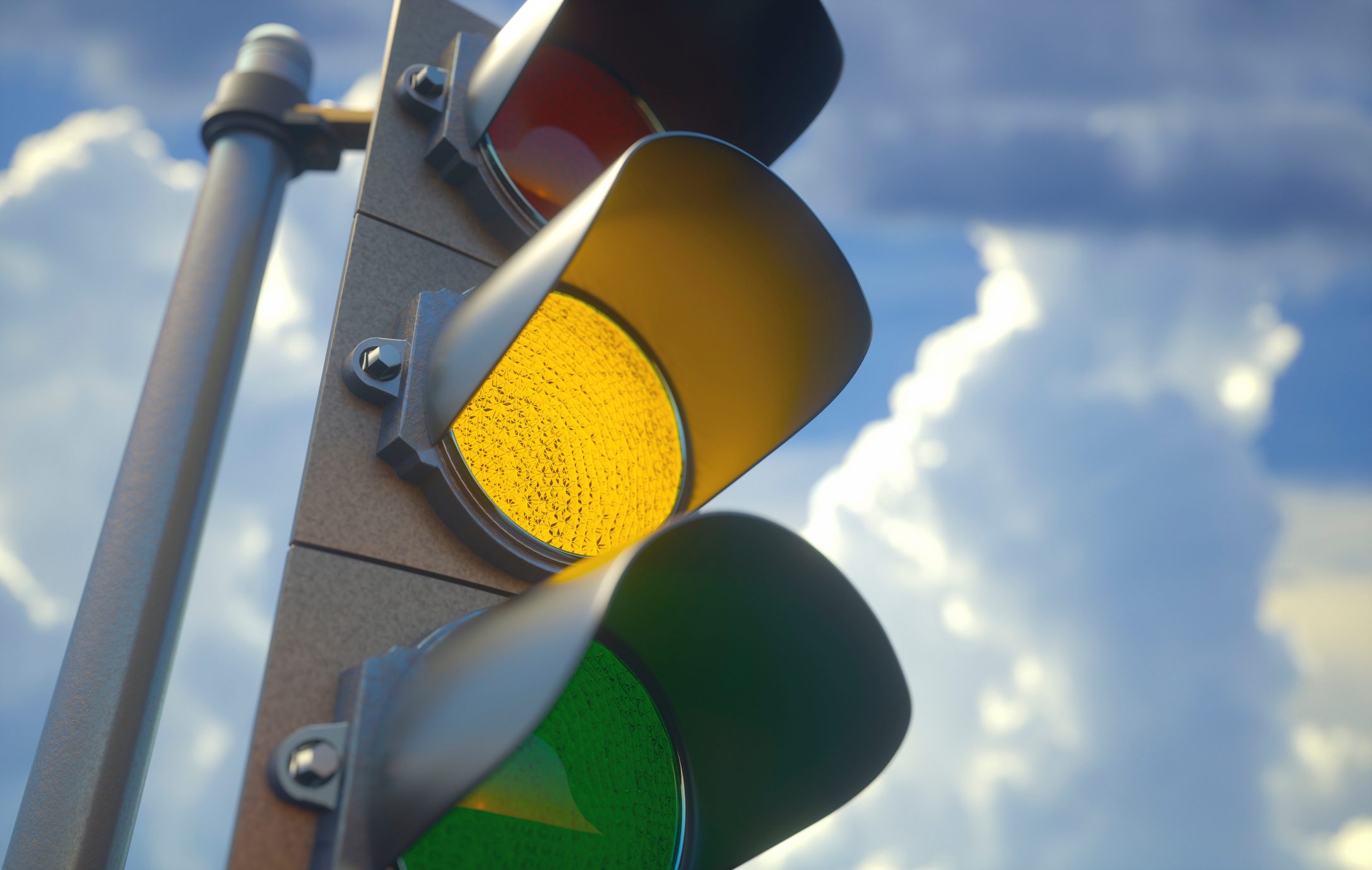 Traffic light displays yellow, indicating caution, with vibrant sky and clouds in the background.