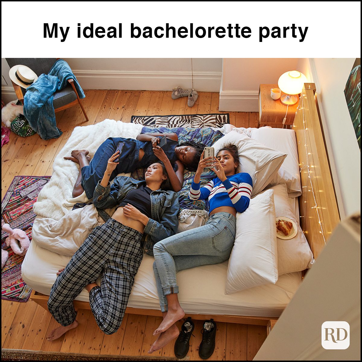 Full length of young female friends using smart phones while relaxing on bed at home during slumber party