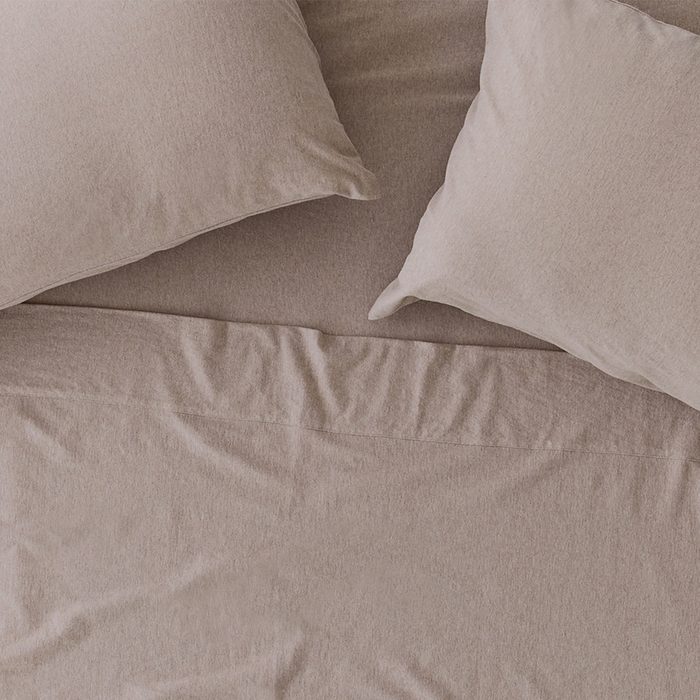 Beige pillows rest on a neatly arranged bed with matching sheets in a soft, cozy bedroom setting.