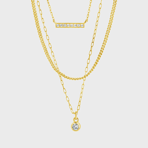 Three gold necklaces layered together; one features a horizontal diamond bar, and another has a small circular diamond pendant; set against a white background.