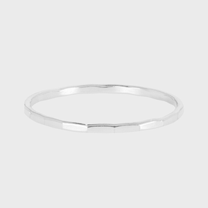 A thin, silver bangle with a faceted design rests on a plain, light gray background.
