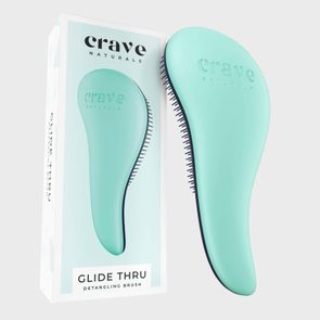 A mint-colored detangling brush, positioned vertically, next to its packaging. Text on the box reads, 