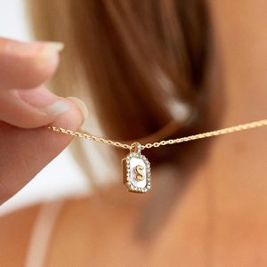 Necklace held by fingers, displaying a gold pendant with the letter 