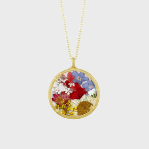 A pendant encases vibrant pressed flowers, hanging from a delicate gold chain, set against a plain white background.