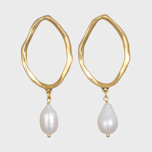 Earrings hang with irregular gold loops and pearl drops; set against a plain gray background.