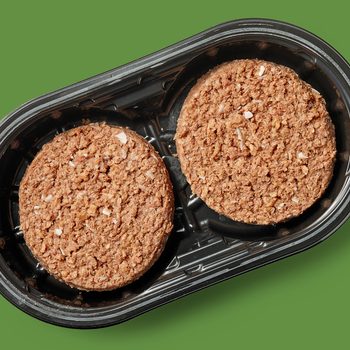 Two brown, textured patties sit in a black plastic tray on a green background.