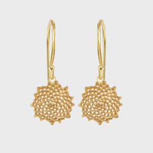 Gold earrings hang, featuring intricate, circular floral patterns in a minimalist white background.