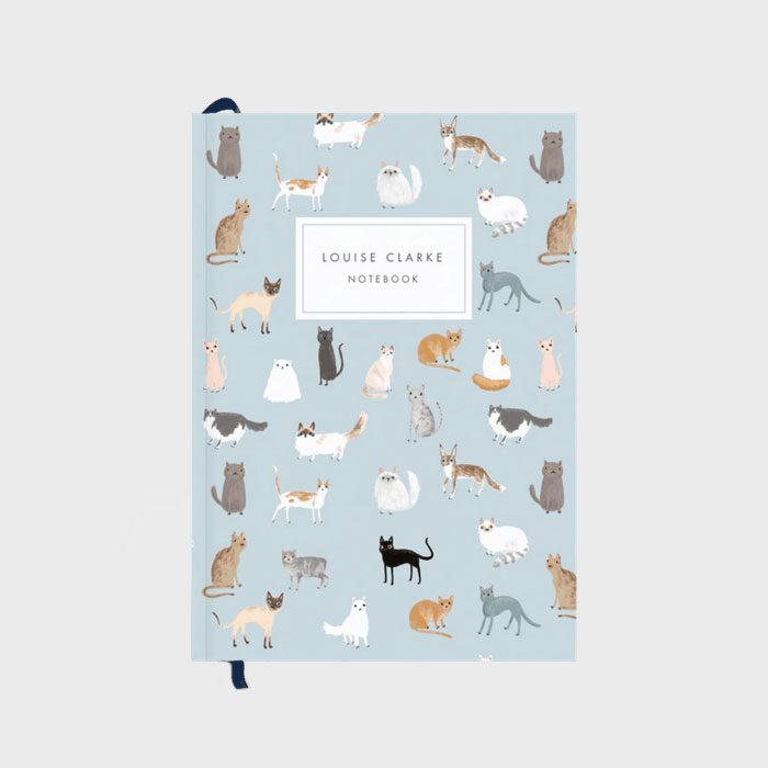 Notebook adorned with various illustrated cats on a light blue cover; features text reading 
