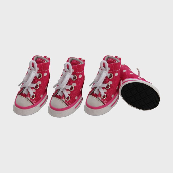 Pink polka-dot sneakers stand arranged in a line; one leans, showing a black sole, against a plain background.