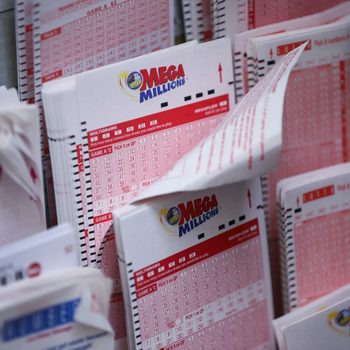 Mega Millions lottery slips are stacked in a display rack, showing checkboxes and numbers in a retail setting.
