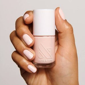 Hand holds pale pink nail polish bottle with logo, 