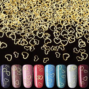 Nail tips display metallic heart-shaped decorations on colorful backgrounds, surrounded by scattered golden heart pieces on a black surface.
