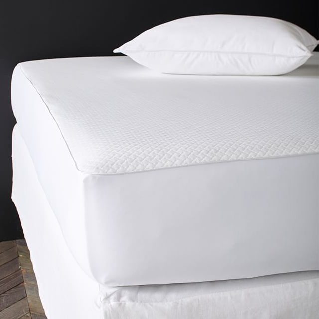 White pillow resting on a neatly made bed with a quilted mattress cover, against a dark background.