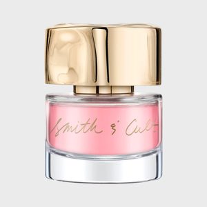 A nail polish bottle displays pink liquid and a gold cap, set against a plain background. Label reads 