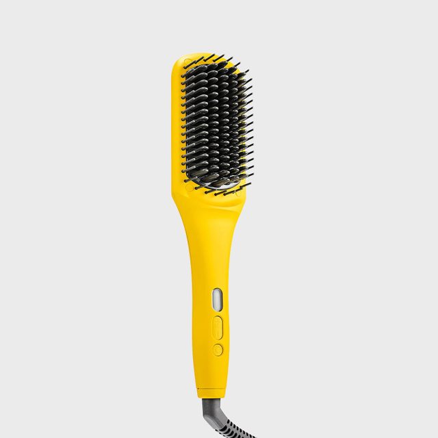 A yellow electric hairbrush with black bristles is positioned upright on a plain gray background.