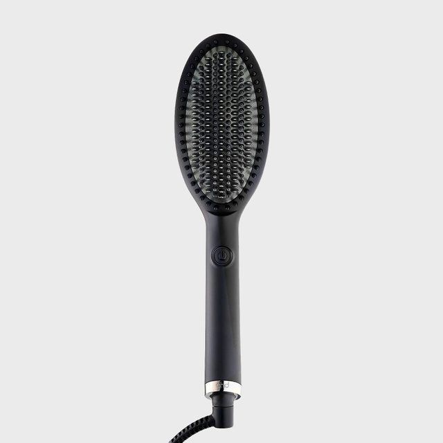 Hairbrush lies upright; bristles arranged symmetrically; sleek, black handle with power button; coiled cord attached; plain light gray background.