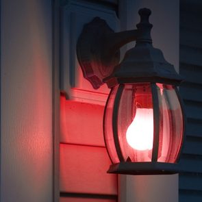 A lantern emits red light, mounted on a wall, casting a warm glow on wooden siding beside closed window shutters.