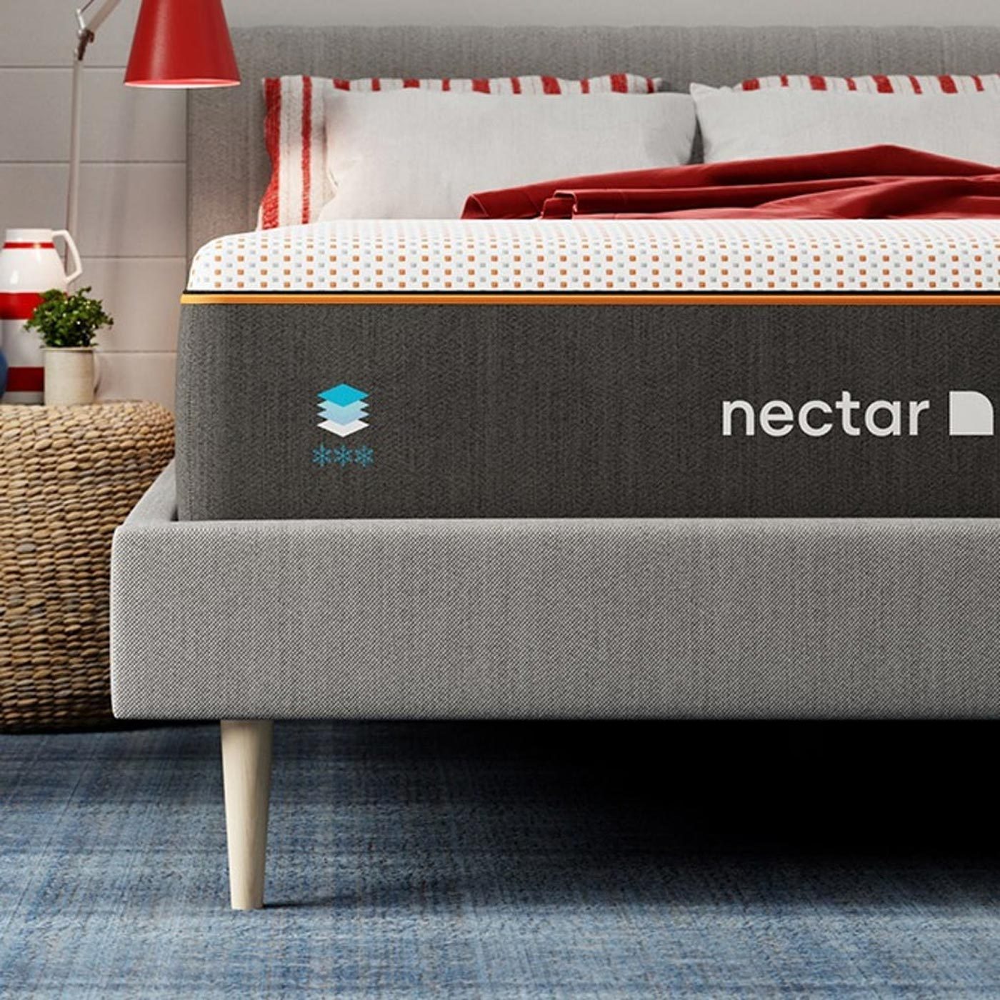 Mattress rests on bed frame; "nectar" logo visible. Nearby, a woven basket and a red lamp enhance a cozy bedroom setting.