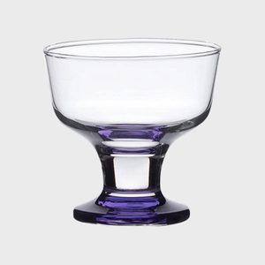 A clear glass dessert bowl sits on a flat surface, featuring a purple base, against a plain gray background.