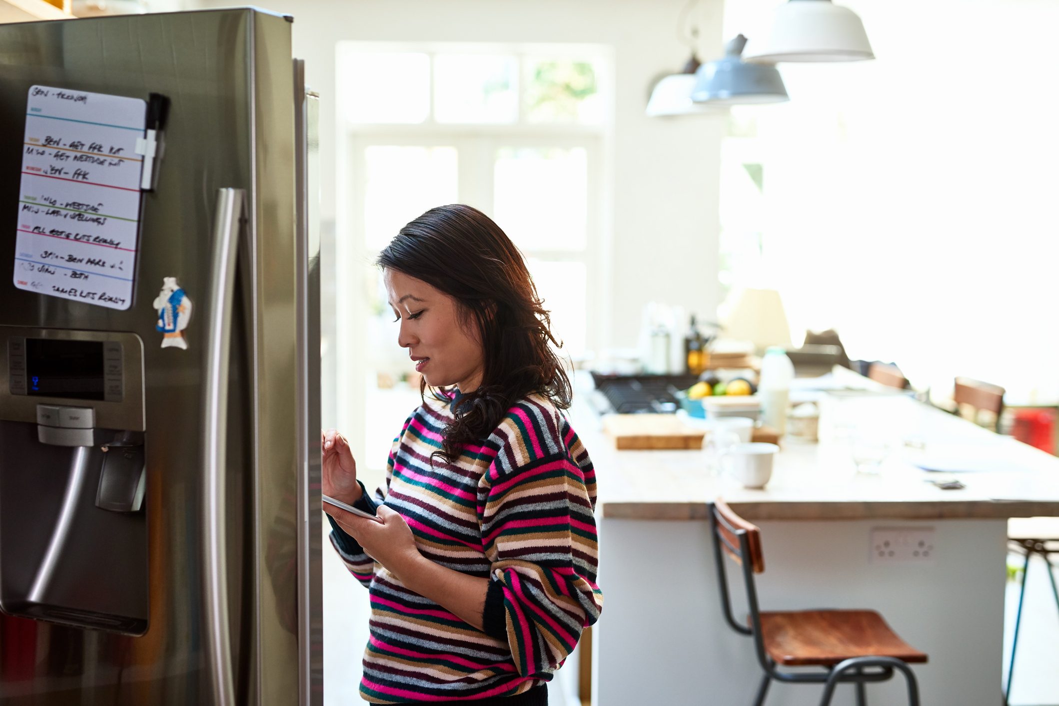 Mid adult woman checking food in fridge holding tablet