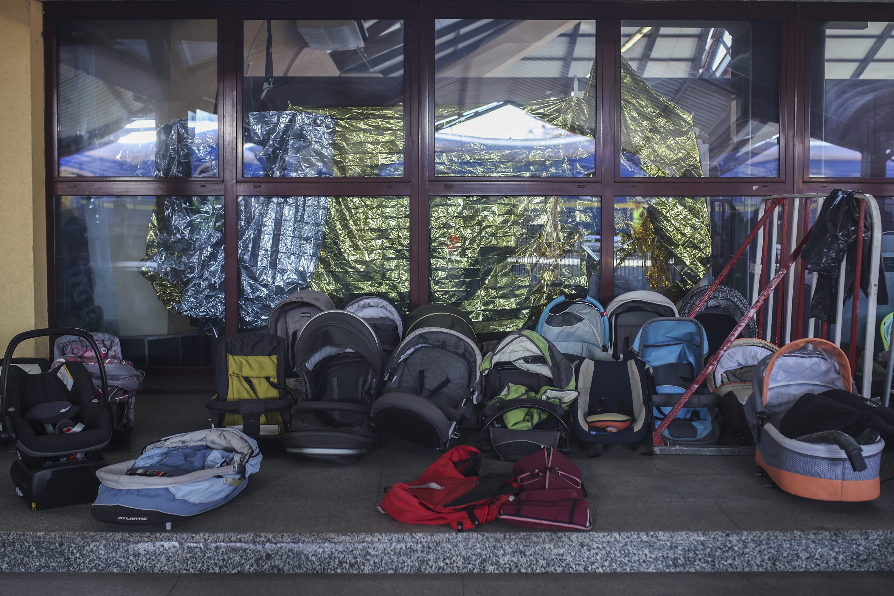 Car seats and carriers sit idle on a concrete floor, backed by a window with shiny material draped outside.