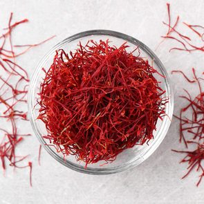 Red saffron threads fill a clear bowl, scattered on a textured white surface.