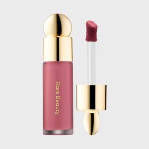 Lip gloss with gold cap shown alongside applicator, against a plain background. Text reads 