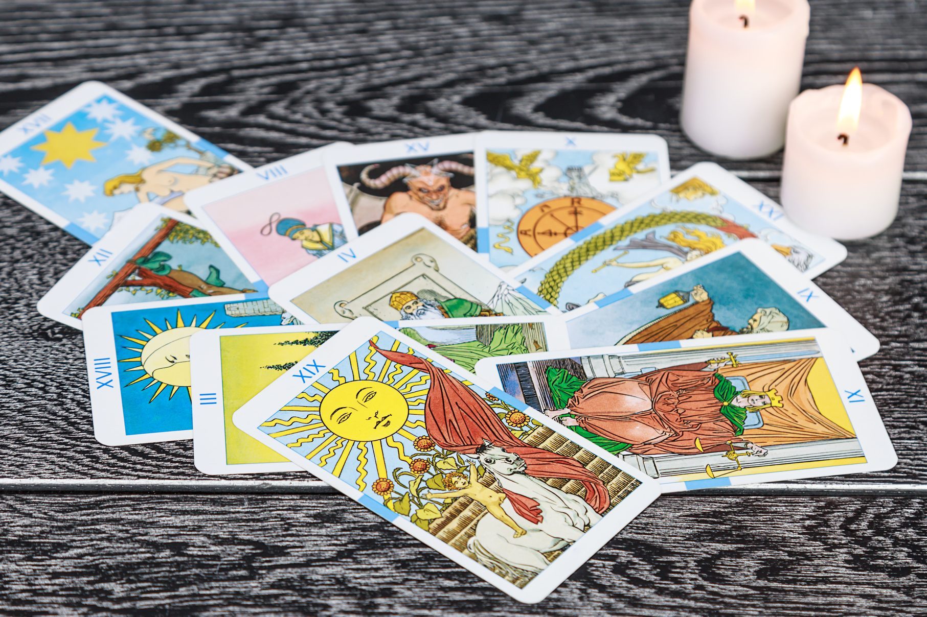 Tarot cards spread across a wooden table with two lit white candles nearby, creating a mystical atmosphere.