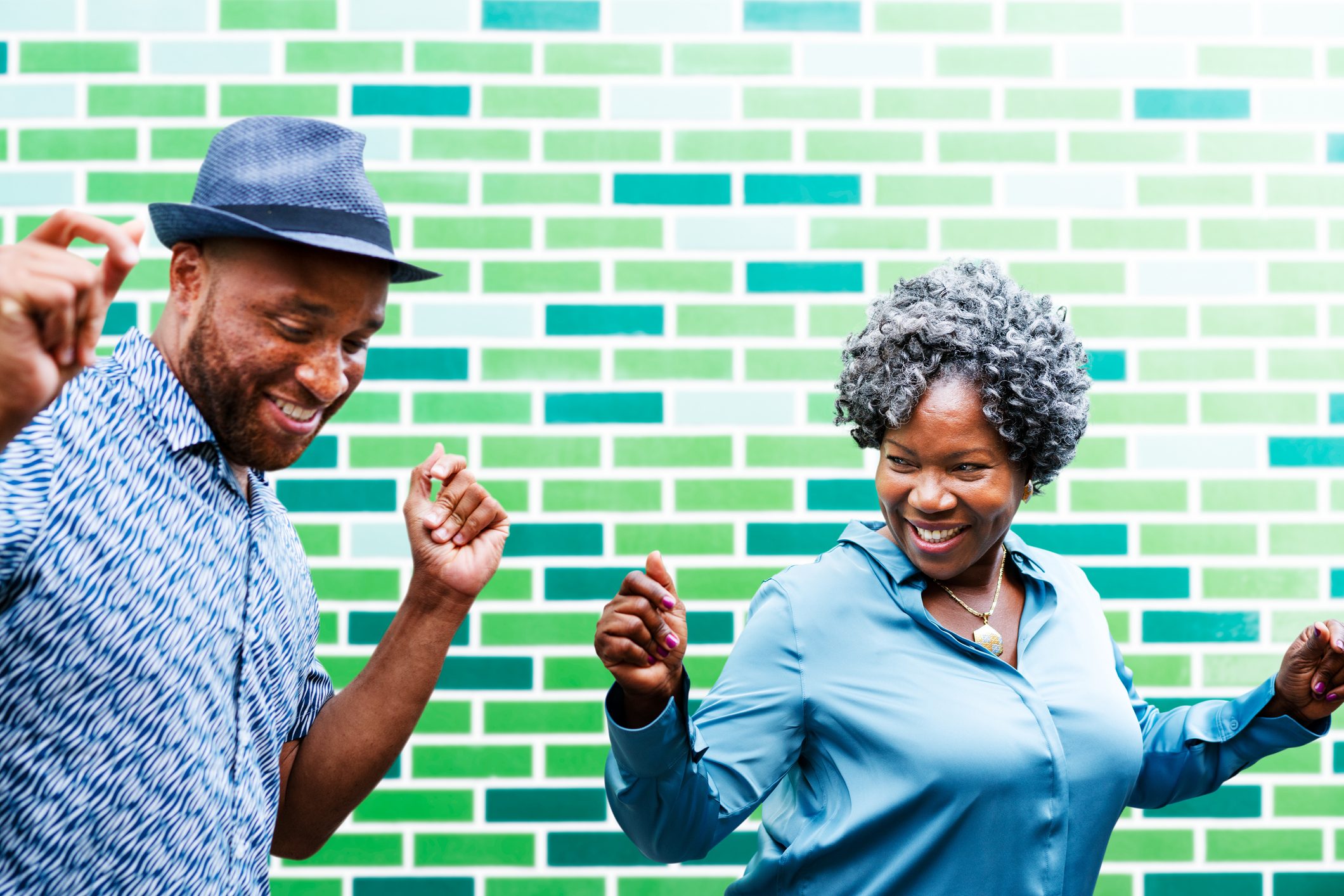 Two people dancing, smiling broadly against a green brick wall.