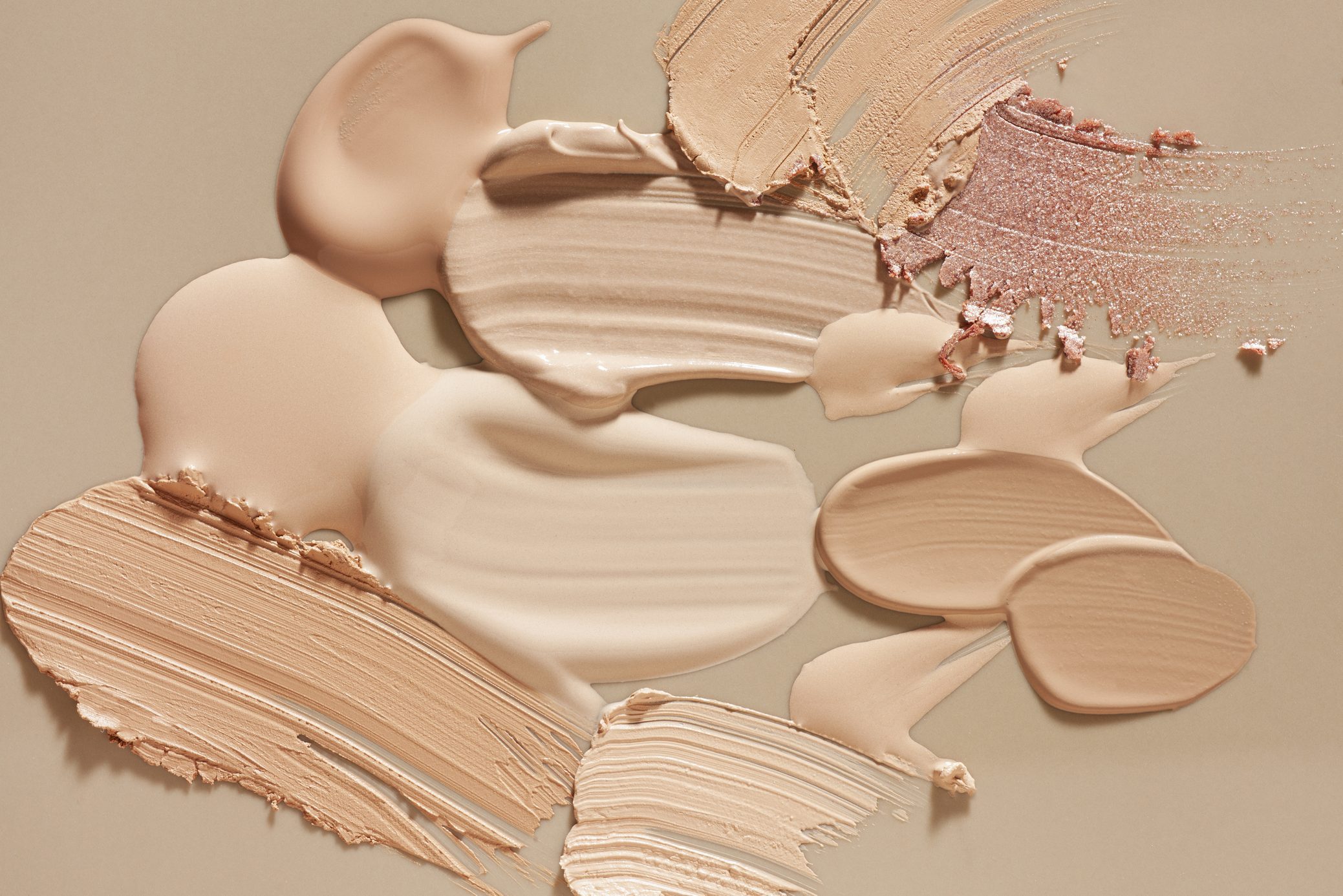 Various shades of creamy makeup swatches blend harmoniously on a neutral beige surface, highlighting their textures and tones.