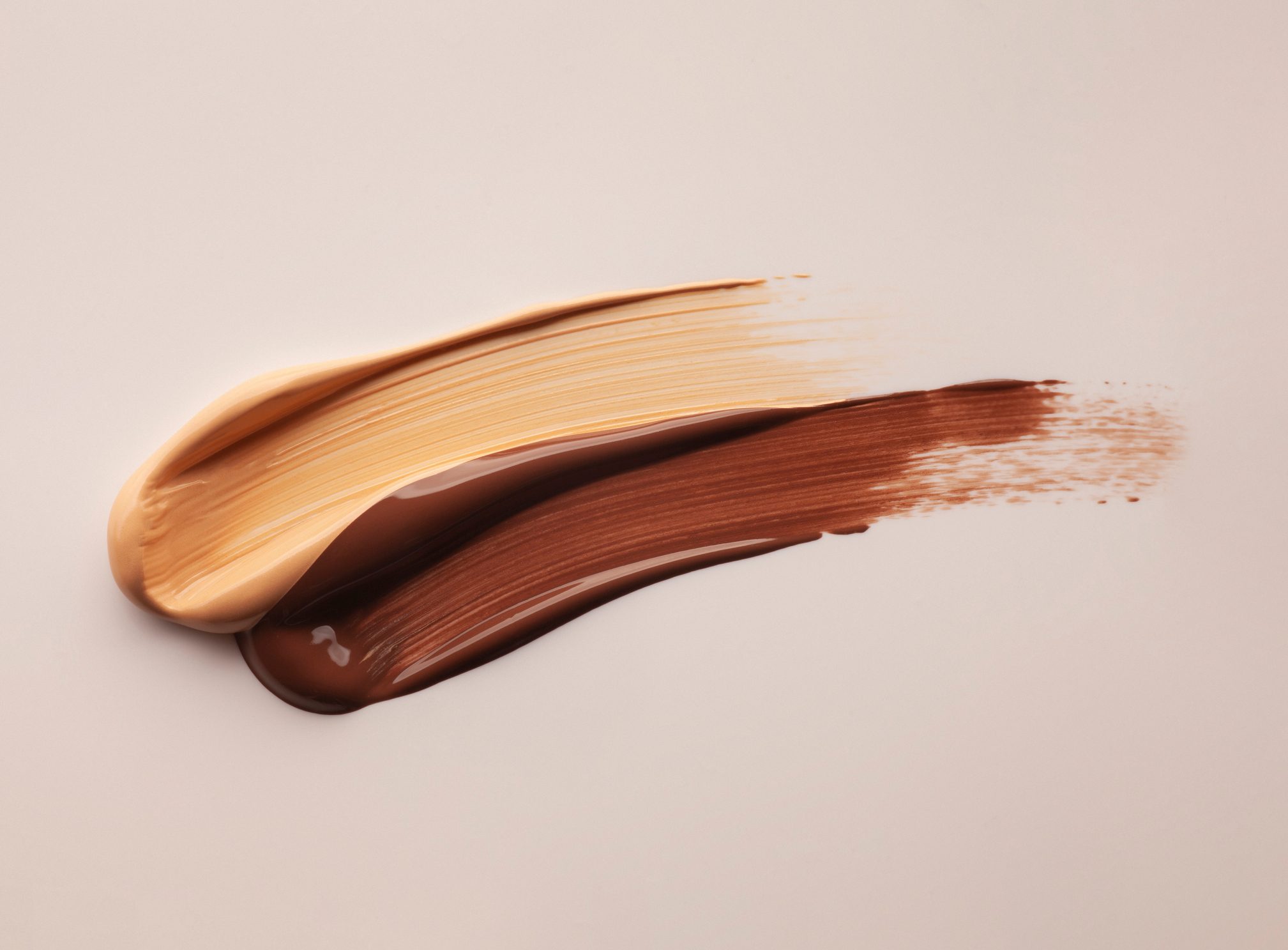 Two overlapping brushstrokes, tan and brown, spread smoothly across a light, neutral background.