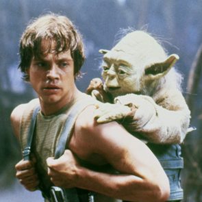 A man carries a small, green creature on his back through a misty, forest-like environment, both looking serious and focused.