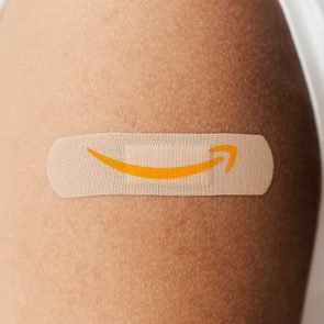 A bandage with an orange Amazon logo is placed on a person's upper arm, against a neutral background.