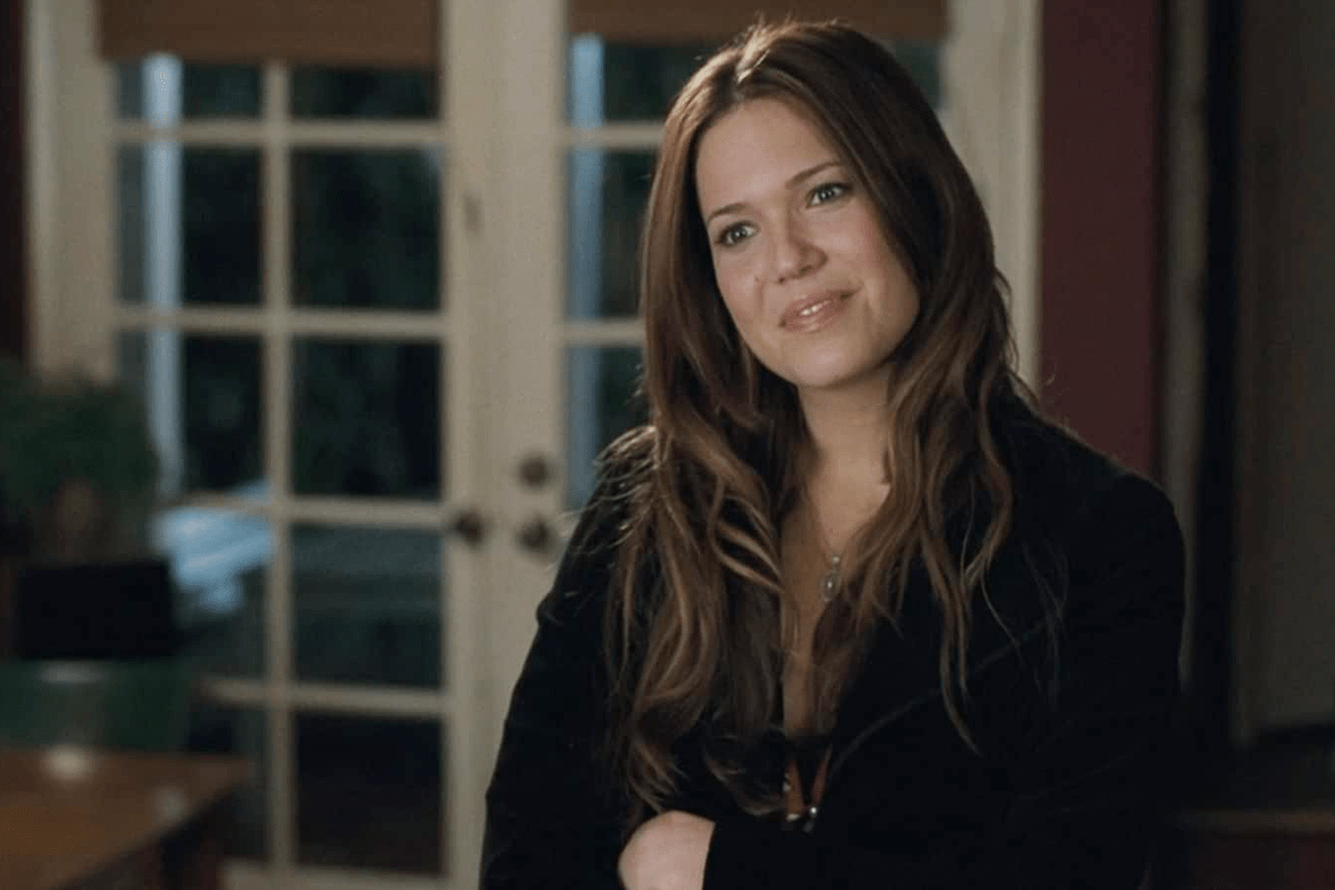 A person stands smiling, arms crossed, inside a room with large glass doors and soft lighting.