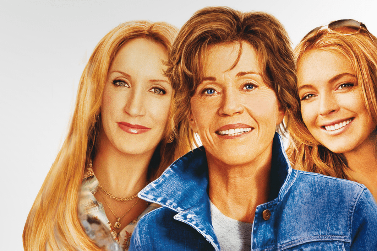 Three women smiling closely together, wearing casual outfits, against a light background.