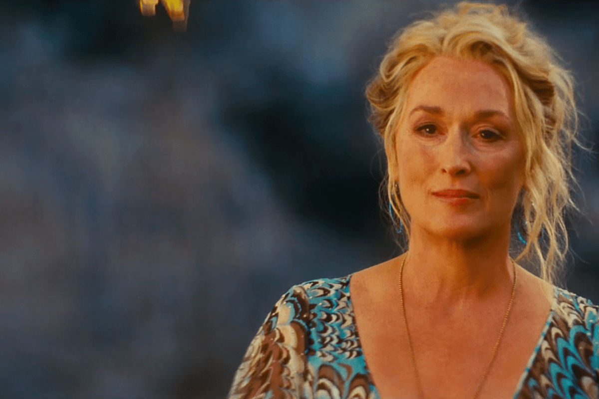 A woman stands calmly, wearing a patterned dress, with a blurred background, giving a serene expression.