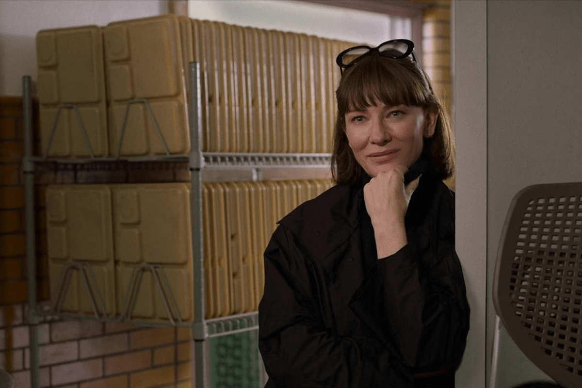 A woman standing, leaning on a surface, in a room with stacked beige containers on metal shelves, wearing glasses on her head.