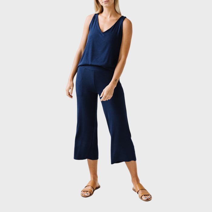 Woman wearing a navy sleeveless top and pants, posing standing on a plain white background, with brown sandals.