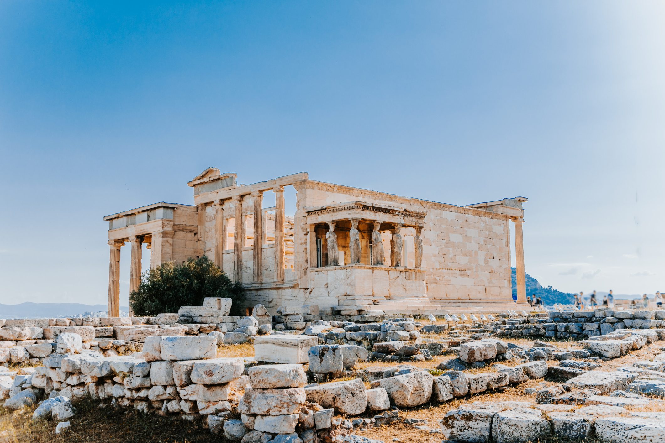 Ancient temple stands silent, surrounded by fragmented stone ruins, under a clear blue sky, evoking a sense of history and timelessness.
