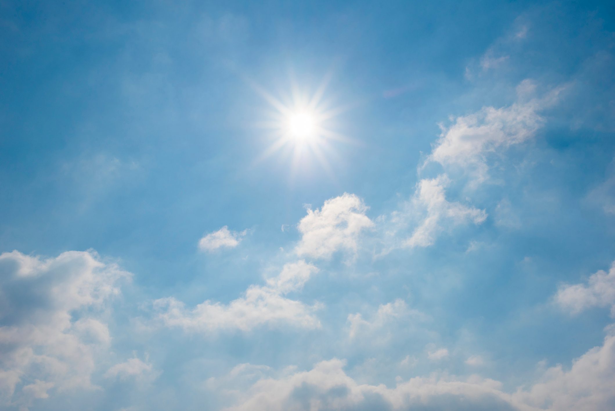 Sun shines brightly, illuminating scattered fluffy clouds in a clear blue sky.