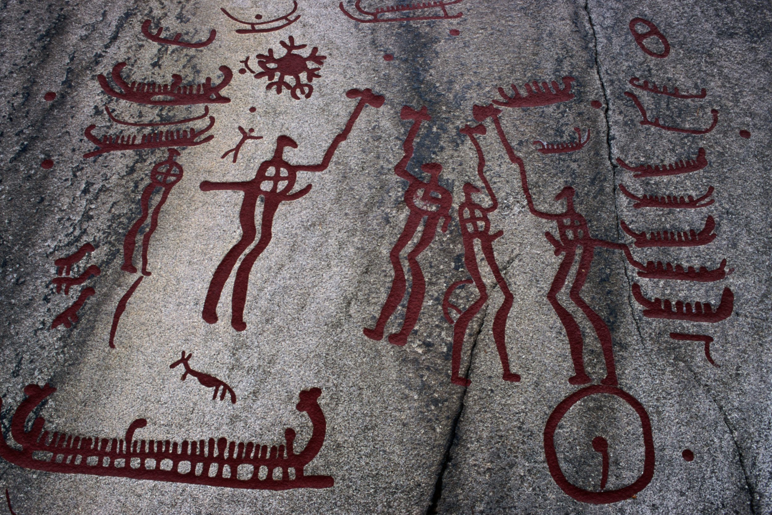 Red petroglyphs depict human figures and boats etched into a gray rock surface, surrounded by abstract symbols.