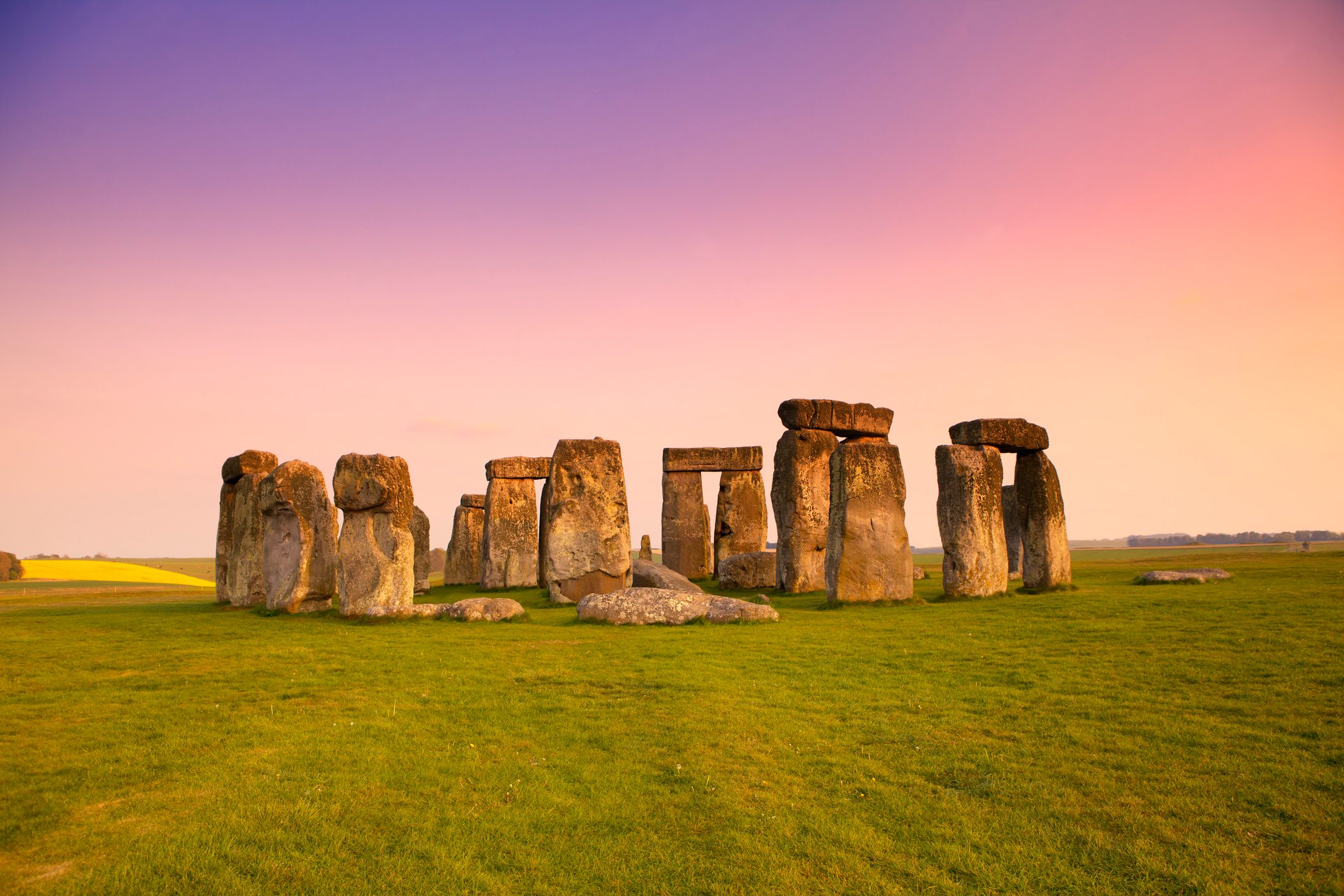 Stonehenge stands still under a colorful sunset, surrounded by a vast grassland.