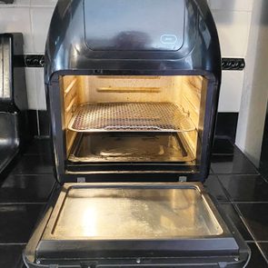 An air fryer oven stands open on a kitchen counter, revealing wire racks inside, beside a stove with visible knobs.