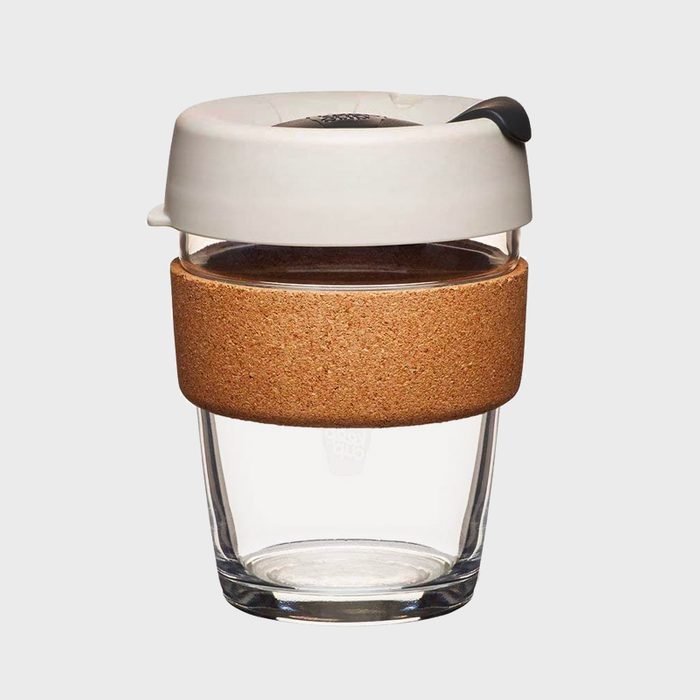 A glass coffee cup features a cork band and white lid, sitting on a plain gray background.