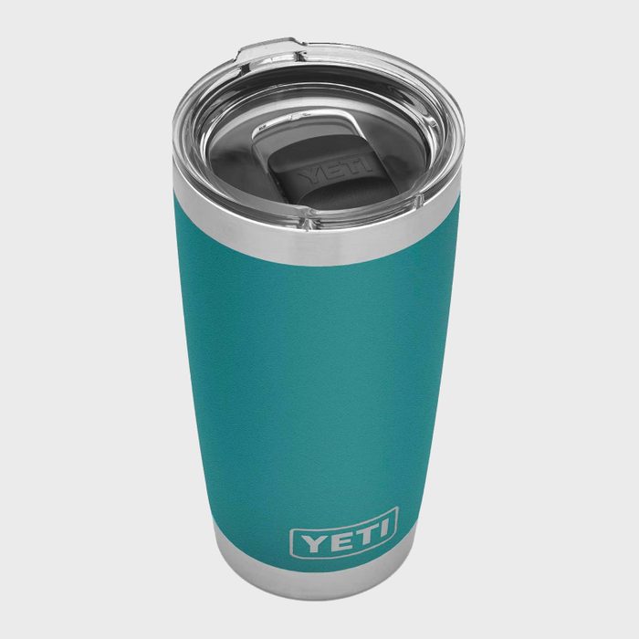 A teal insulated tumbler with a clear lid rests upright on a plain surface, displaying the logo 