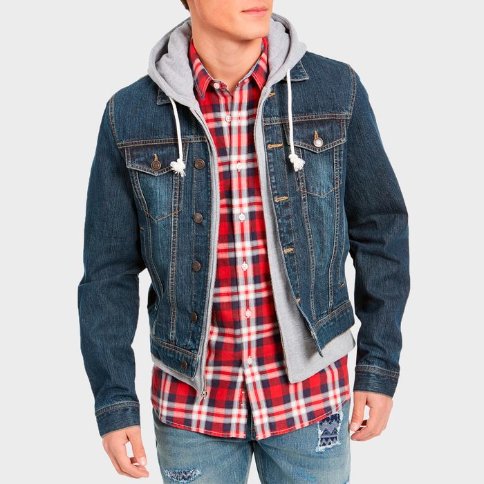 Person wearing a denim jacket over a gray hoodie, with a red plaid shirt, stands against a plain background.