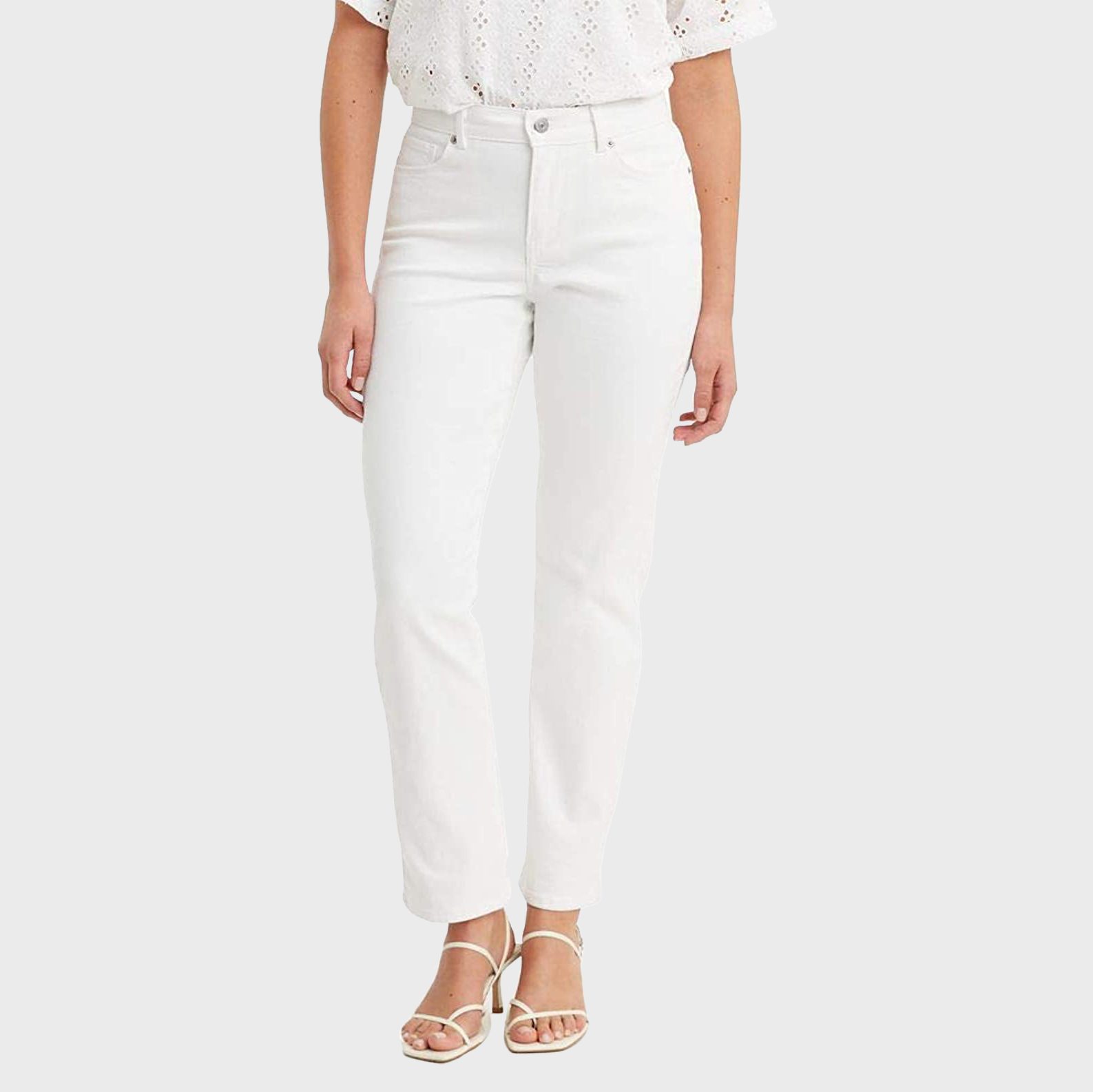 A person stands wearing white jeans and strappy sandals against a plain white background.