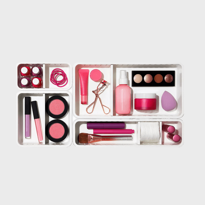 Cosmetics are organized within white trays, featuring lip glosses, blush, brushes, and a beauty blender, creating a tidy and colorful arrangement.