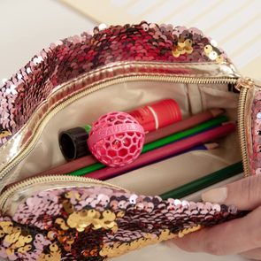 A sequined pouch contains colored pencils, a pink ball labeled 